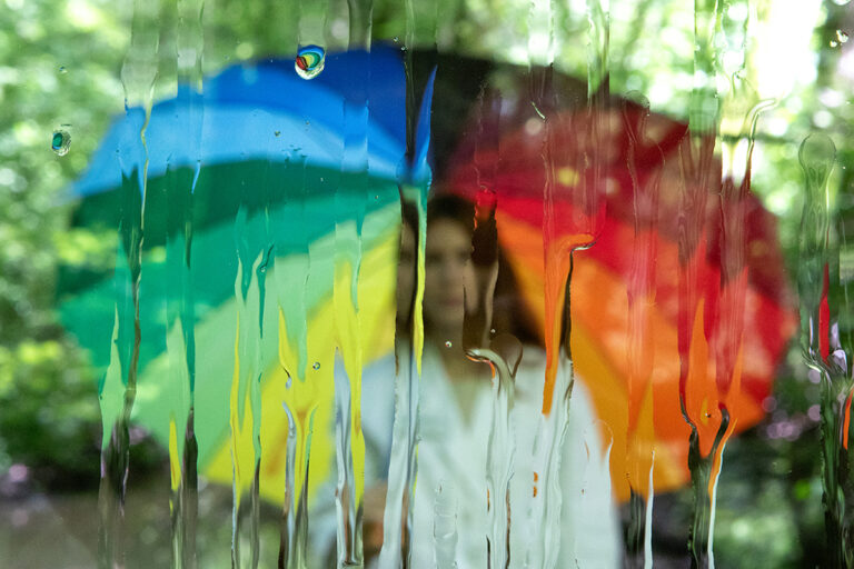 Junge Frau unter einem regenbogenfarbigen Schirm.